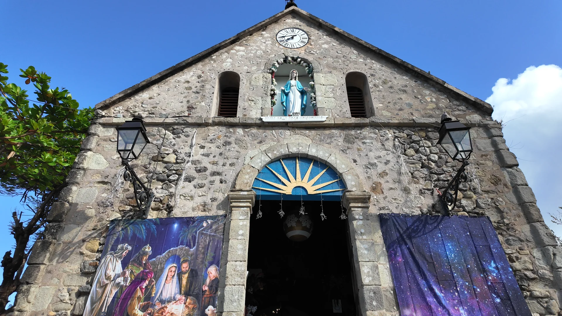 Façade en pierre de l'église de Terre-de-Haut, horloge, statue et entrée bleue